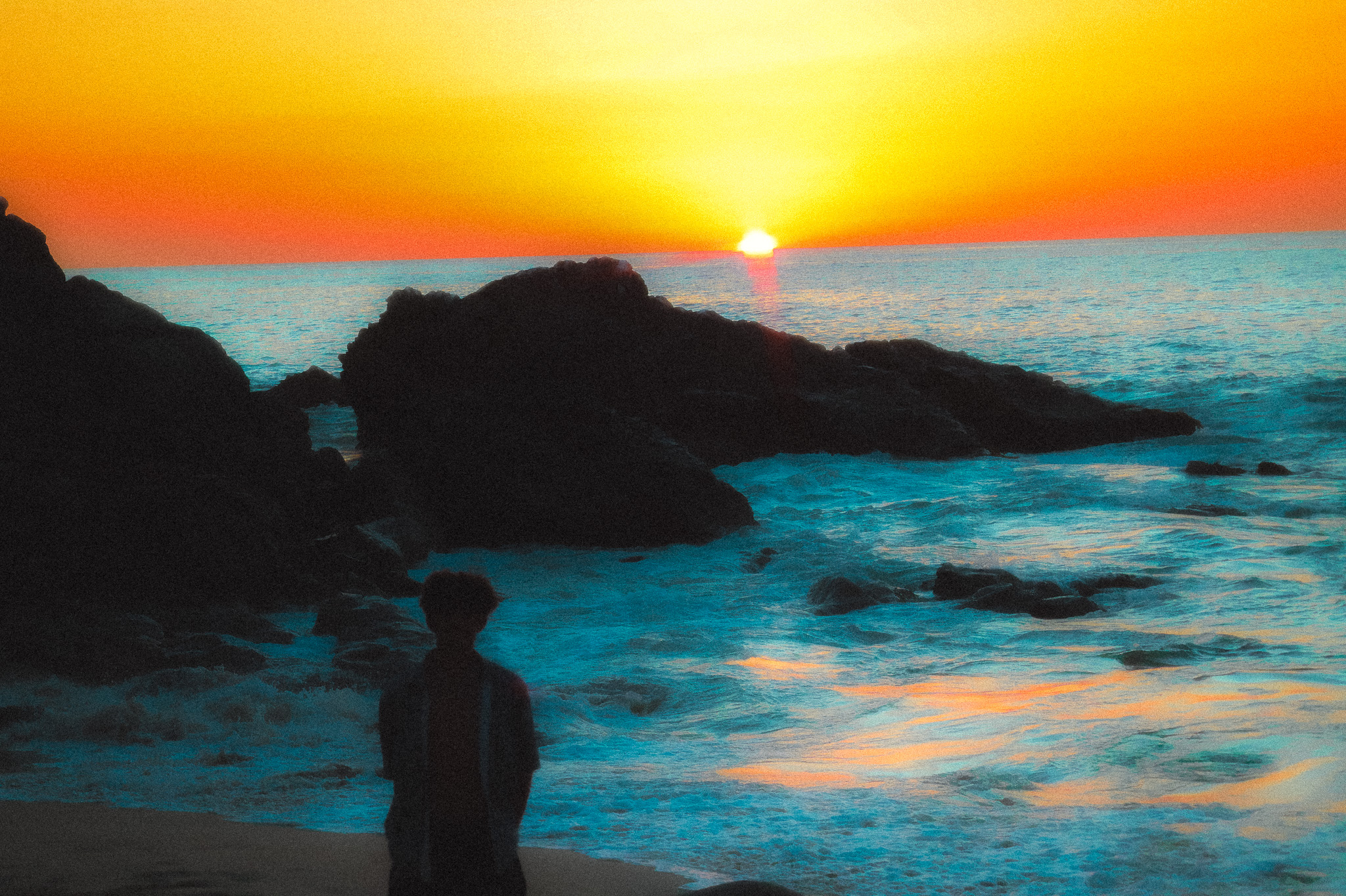Figure standing on a rocky coast at sunset in grayscale